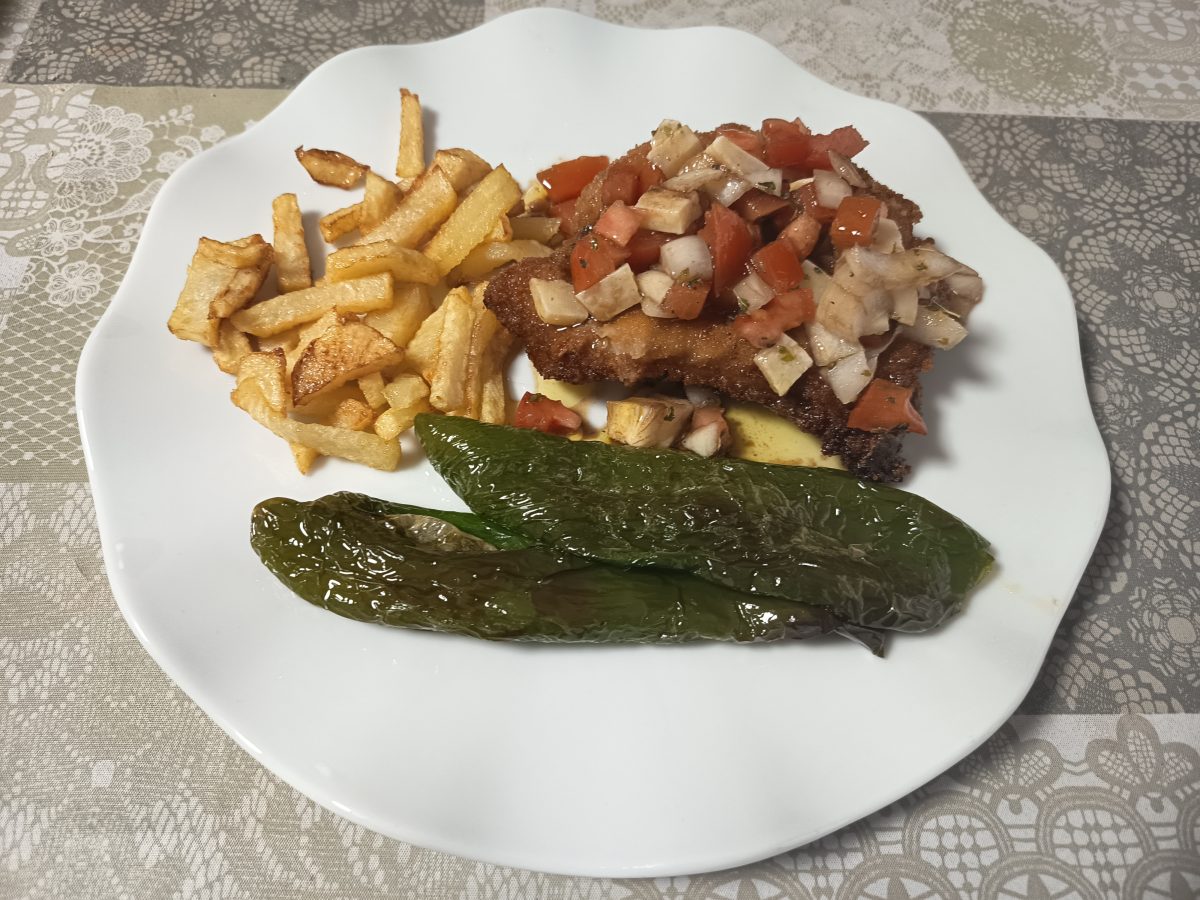 Receta de chuleta de cerdo a la italiana puesta en un plato llano con guarnición de pimientos verdes y patatas fritas.