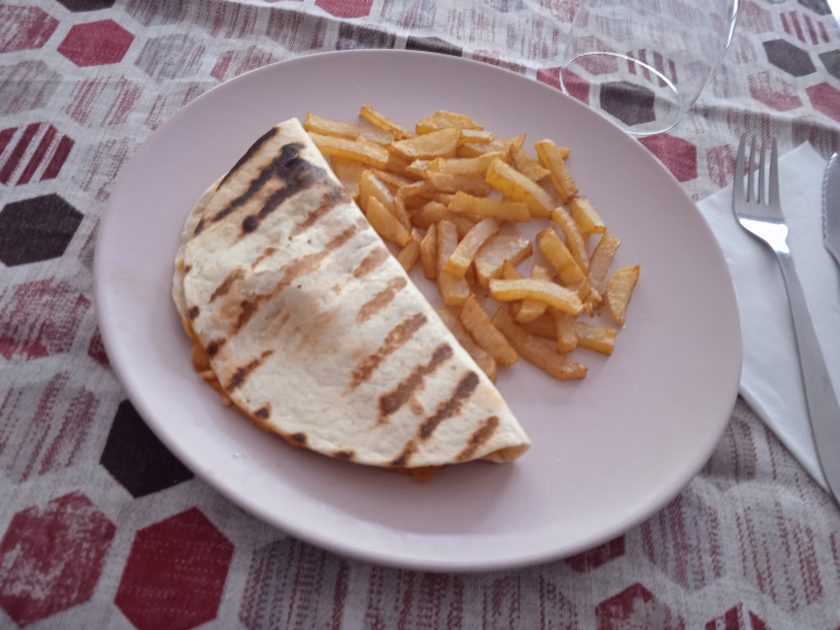 Receta de quesadilla de pollo acabadapuesta en un plato llano de color rosa sobre un mantel con rombos de color rojo y blancos