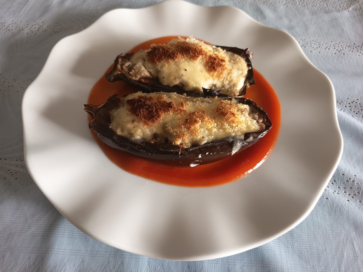 Receta de berenjenas rellenas acabadas puestas en un plato llano de color blanco con una base de salsa de tomate.