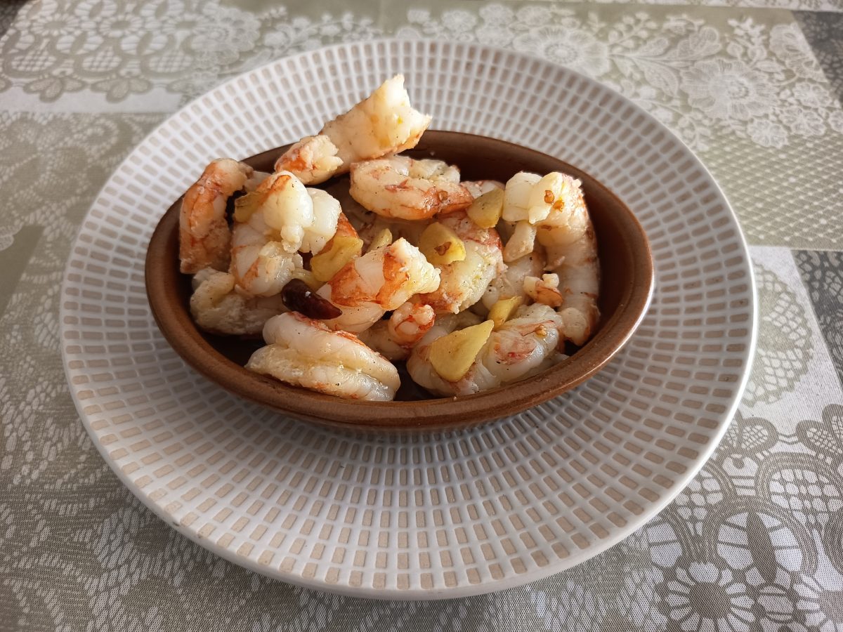 Receta de gambas al ajillo acabadas y puestas en una cazuelita de barro alargada.