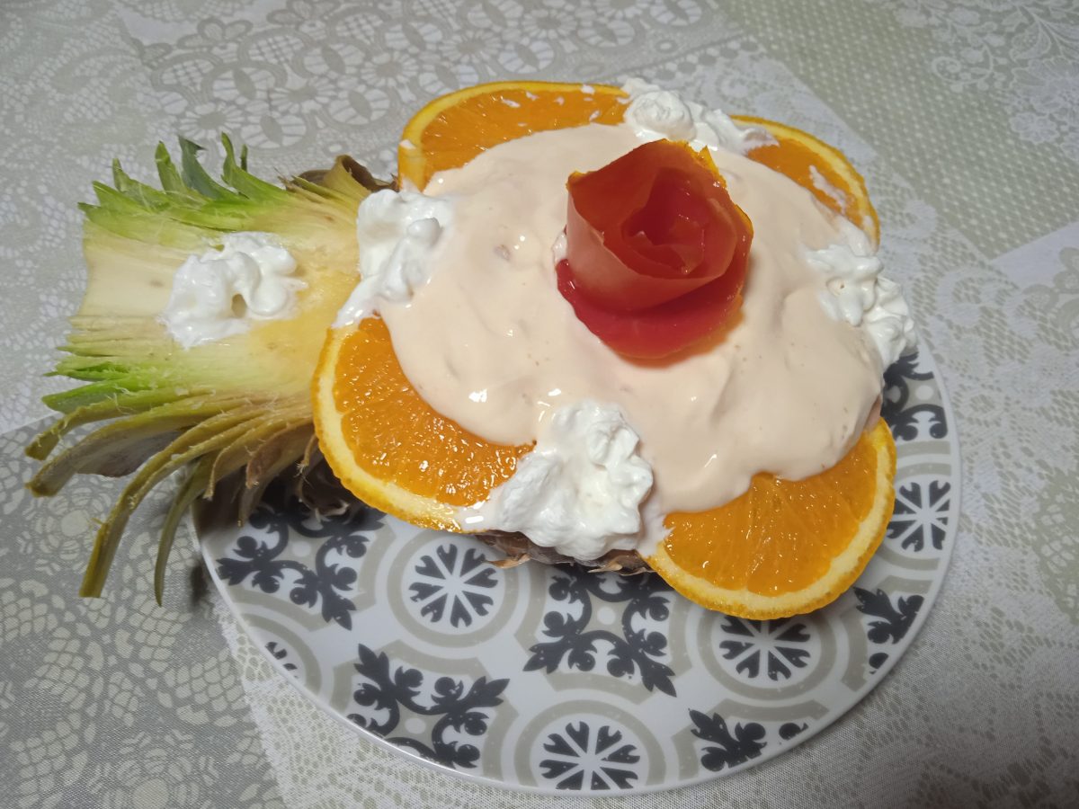coctel de piña acabado cubierto con salsa rosa alrededor medias rodajas de naranja y unos puntos de nata en el centro una rosa de tomate