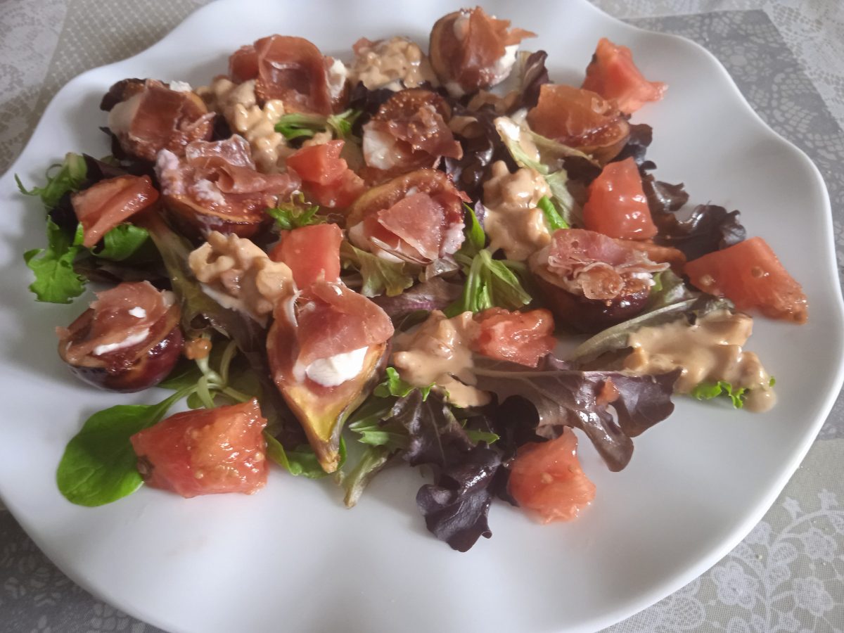 Ensalada de higos con queso de cabra y jamón serrano acabada puesta en un plato llano de color blanco.