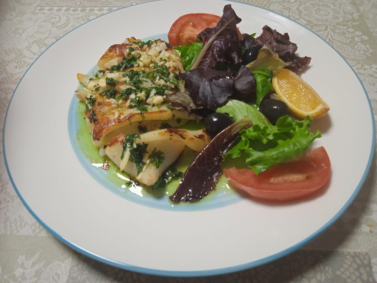 Calamares a la plancha con ajo y perenil acabados puesto en un plato llano con ribete azul y una guarnicion de ansalada en el lado opuesto.