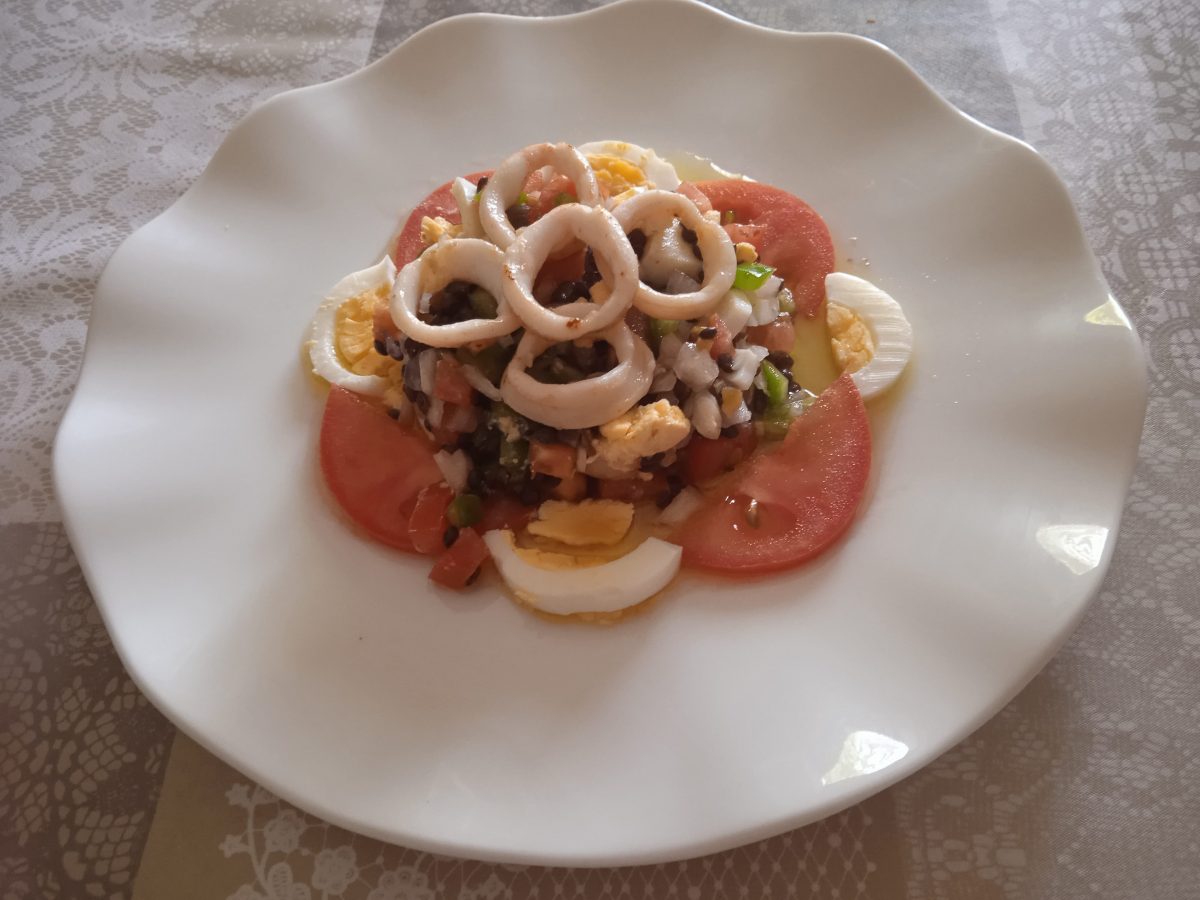 Receta de ensalada de lentejas negras con calamares acabada puesta en un plato llano de color blanco.