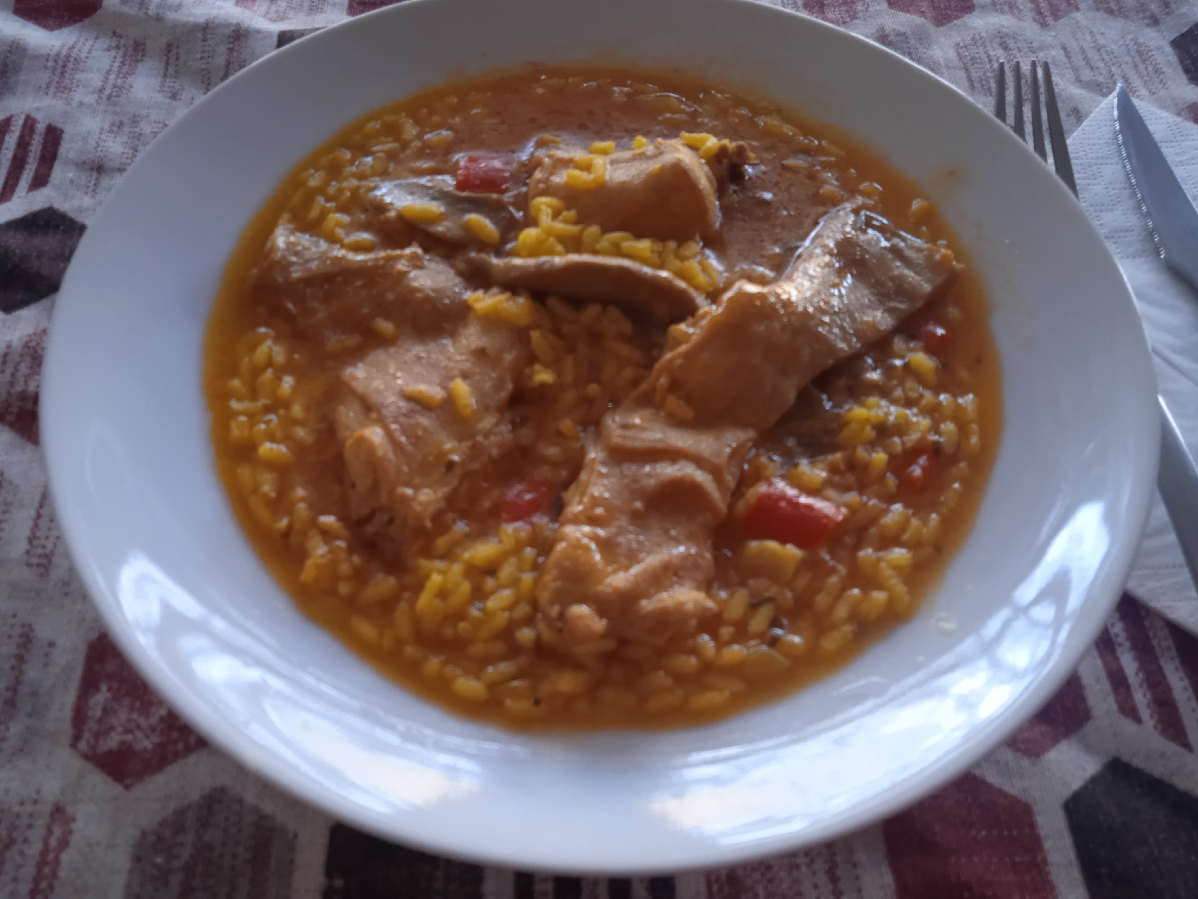 Receta de arroz con conejo y champiñones acabada, puesta en un plato hondo de color blanco, puesto sobre un mantel con rombos