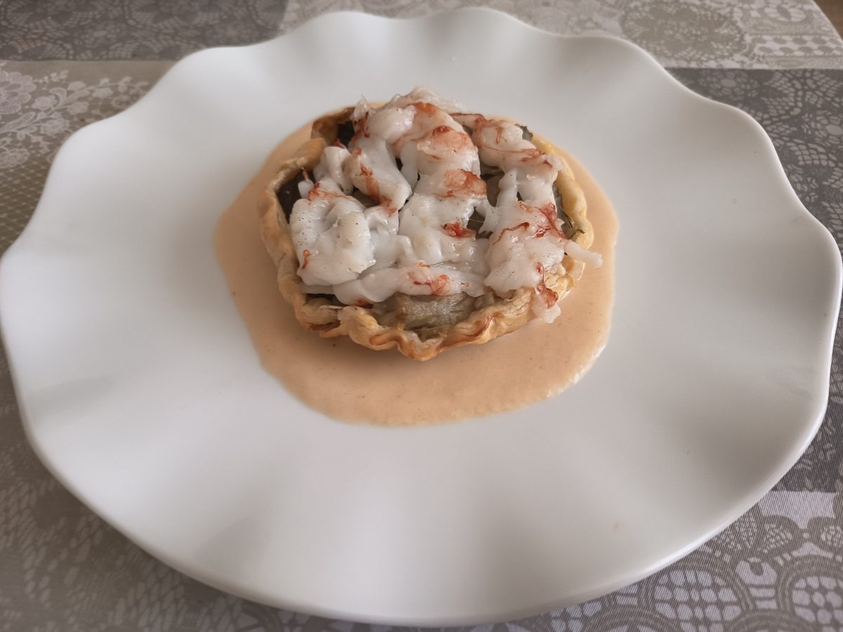 Receta de tarta tatin de alcachofas con gambas acabada puesta en un plato llano de color blando con la salsa en la base del mismo y la tarta tatin de alcachodas encima.