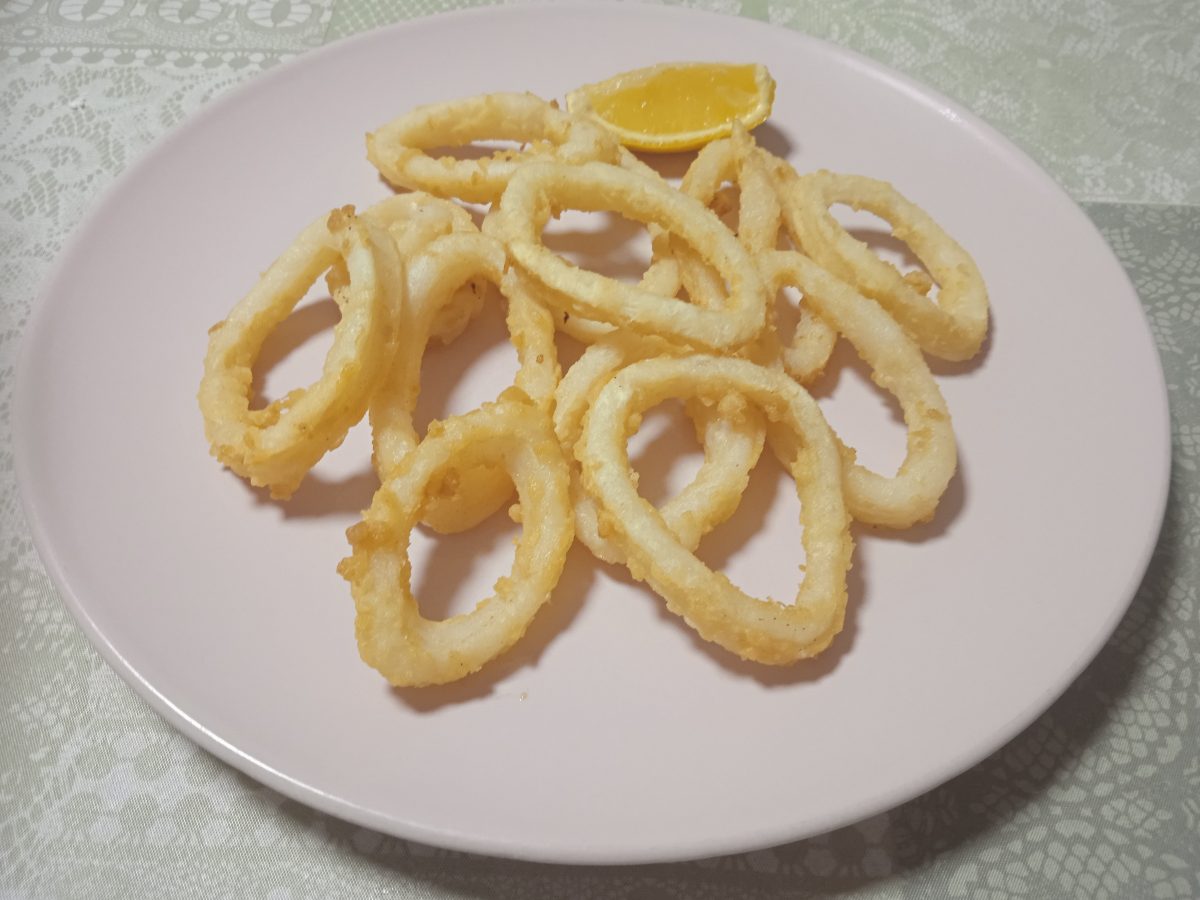 receta de calamares a la andaluza acabados puesto en un plato llano de color rosa con un trozo de limón.
