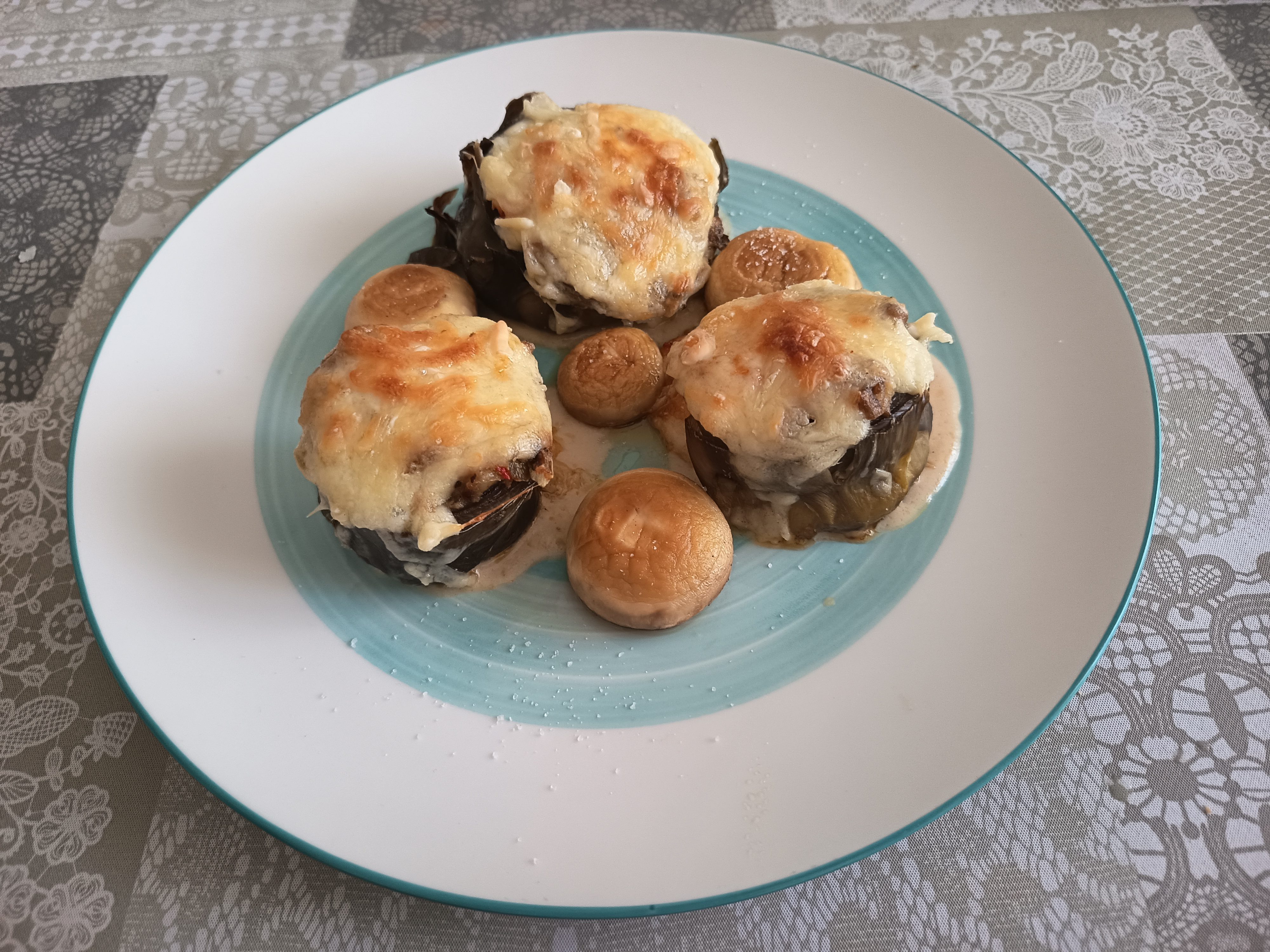 Receta de alcachofas rellenas gratinadas puestas en un plato llano con unos champiñones hechos a la plancha.