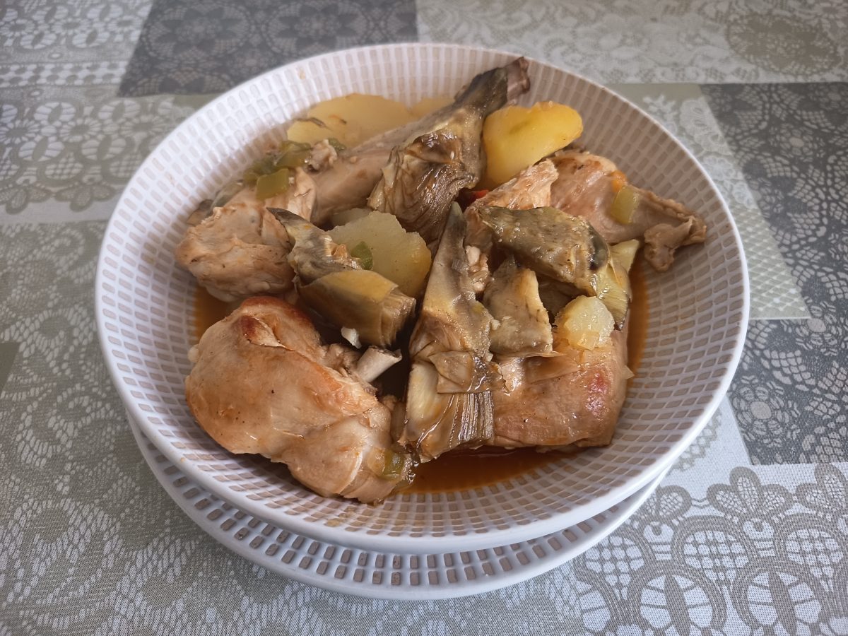 Receta de patatas con conejo y alcachofas acabada y puesta en un plato llano para servirlas.