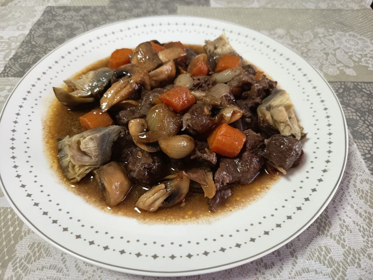 Receta de estofado de ternera al vino tinto acabada puesto en un plato llano de color blanco con ribetes alrededor.