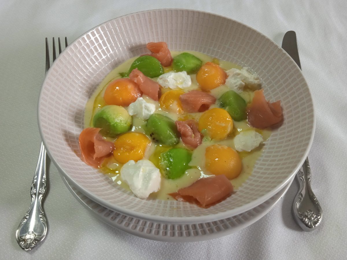 Receta de sopa de frutas con salmón ahumado y queso crema acabada puesta en un plato hondo.