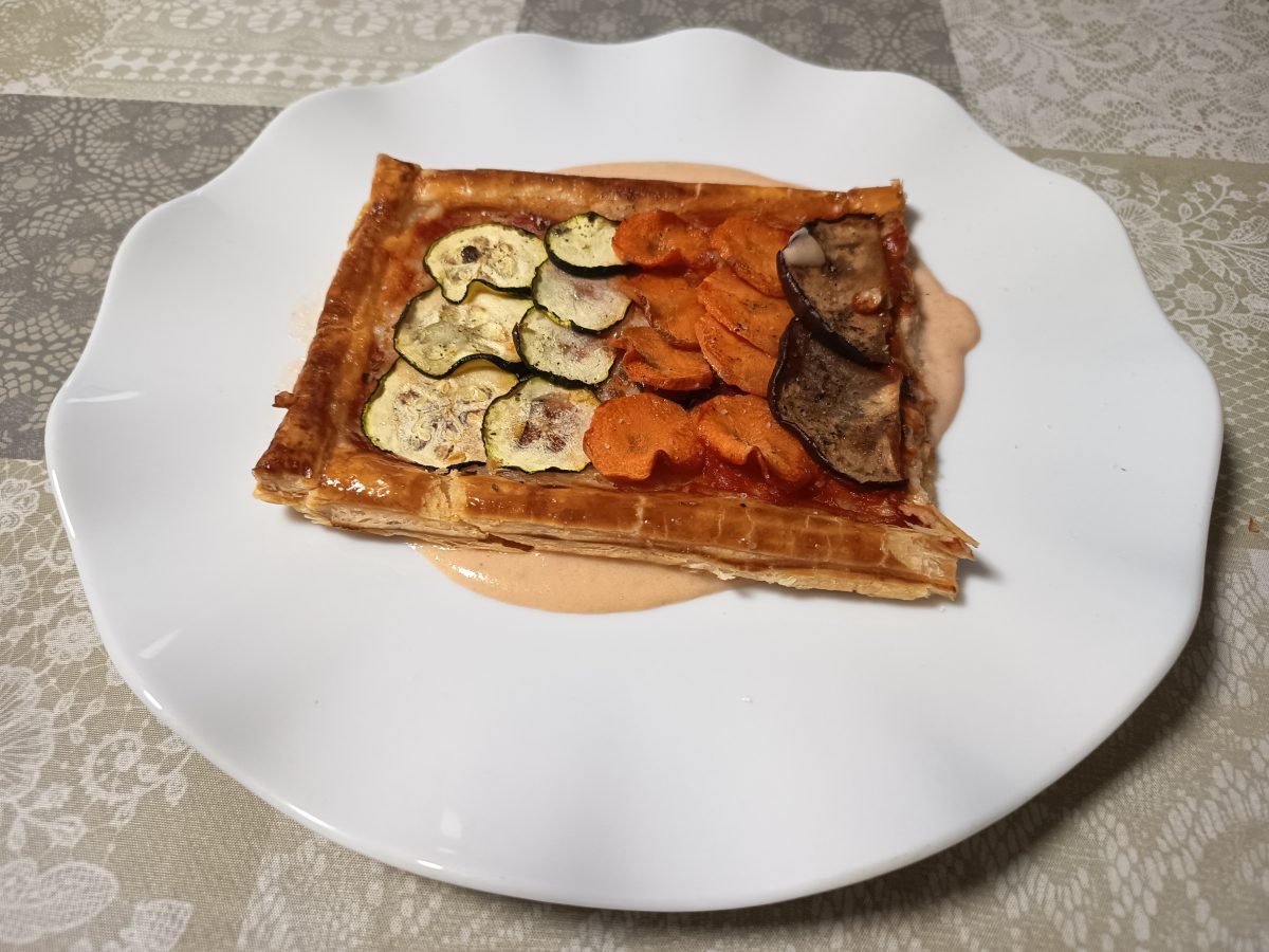1/2 plancha de hojaldre crujiente con verduras horneada puesta en un plato con una base de salsa de tomate y nata líquida lista para servir.