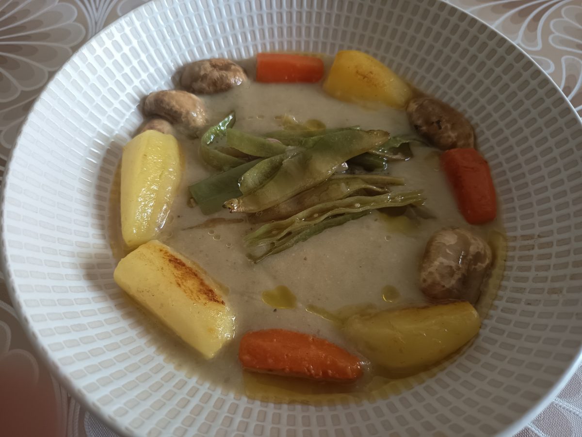Receta de la crema de verduras tíbia acabada puesta en un plato hondo con las verduras salteadas alrededor del plato.