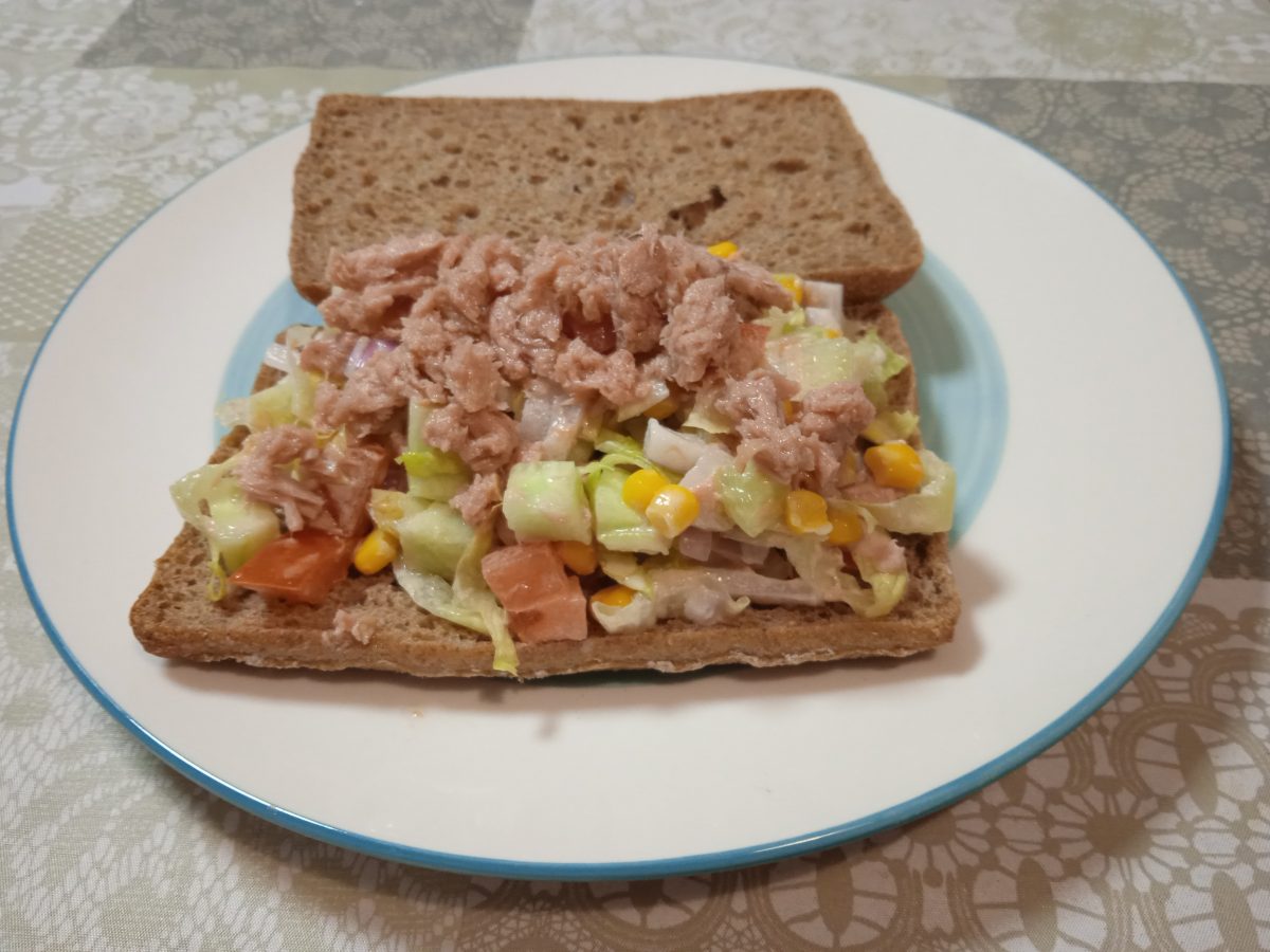 Bcadillo vegetal de atún acabado puesto en un plato llano y abierto donde se ven todos los ingredientes del mismo.