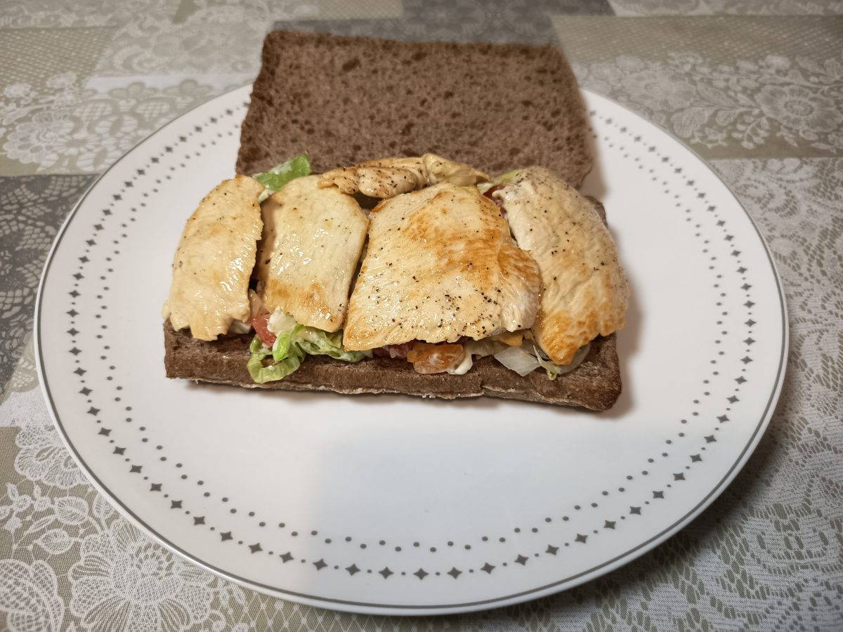 bocadillo de pollo con vegetales puesto en un pan integral que ponemos en un plato abierto.