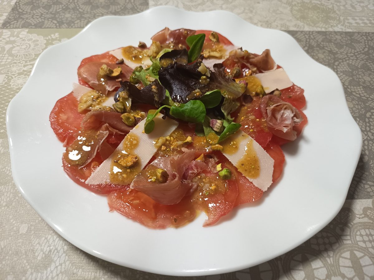 carpacho de toamte con parmesano jamón serrano acabado puesto en un plato llano de color blanco