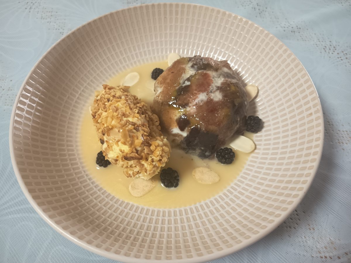 receta de brevas relleno de nata crema y nutella puesto en un plato hondo con una base de crema catalana y un helado rebozado con granillo de almendra y unas moras negras y láminas de almendra alrededor.