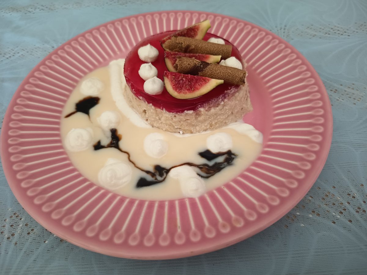 Receta de la mousse de higos acabada puesta en un plato de postres de color rosa con un poco de natillas con caramelo líquido para decorar.