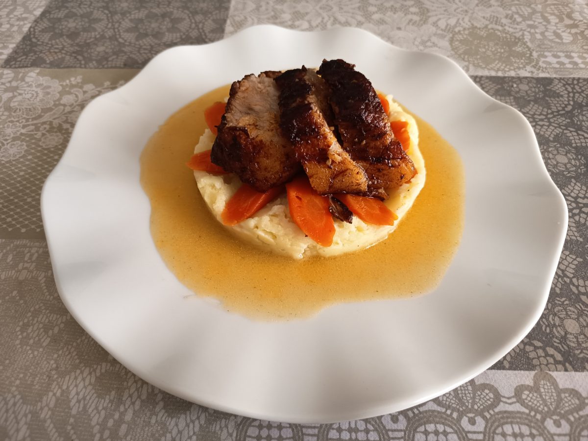 Receta de papada de cerdo acabada puesta en un plato llano sobre puré de patatas y zanahorias cortadas